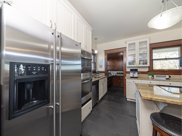 kitchen featuring stainless steel appliances, light stone countertops, white cabinetry, and hanging light fixtures