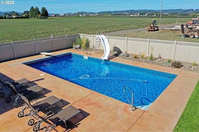 view of swimming pool featuring a rural view, a water slide, a diving board, a mountain view, and a yard