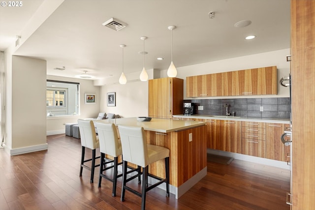 311 NW 12th Ave Unit 602, Portland, OR 97209 - kitchen featuring dark wood-style flooring, a center island, tasteful backsplash, a breakfast bar, and brown cabinets