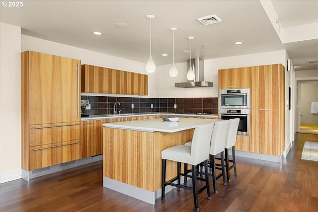 311 NW 12th Ave Unit 602, Portland, OR 97209 - kitchen with wall chimney exhaust hood, modern cabinets, dark wood finished floors, a kitchen island, and brown cabinetry