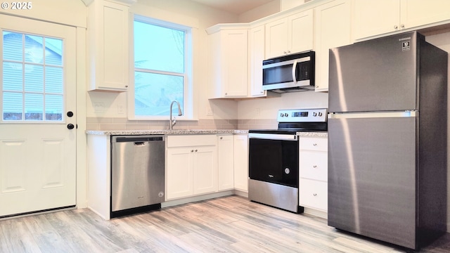 kitchen featuring appliances with stainless steel finishes, sink, light hardwood / wood-style floors, white cabinetry, and plenty of natural light