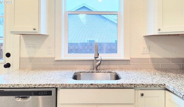 kitchen featuring light stone countertops, tasteful backsplash, stainless steel dishwasher, sink, and white cabinets