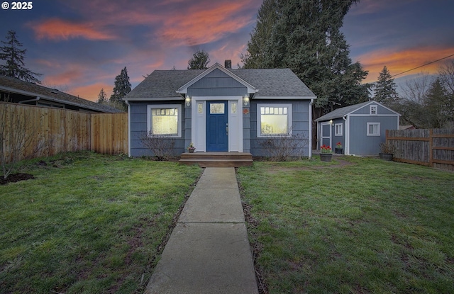 bungalow-style house featuring an outbuilding, a front lawn, a fenced backyard, and a shingled roof