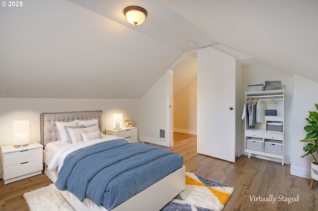 bedroom with visible vents, light wood-type flooring, baseboards, and vaulted ceiling