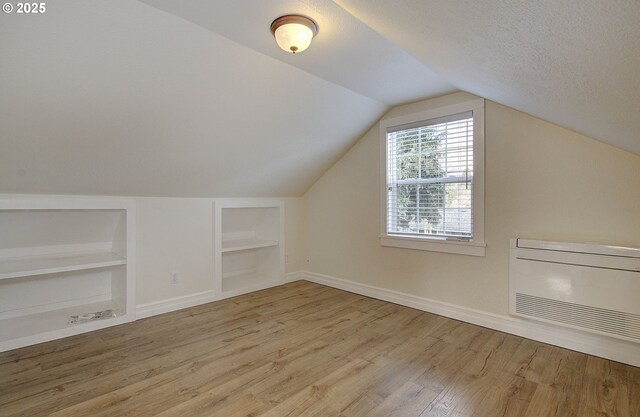 additional living space featuring baseboards, built in features, vaulted ceiling, wood finished floors, and a textured ceiling