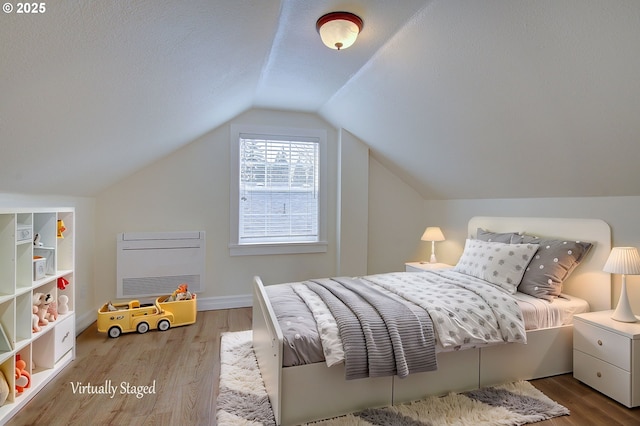 bedroom with vaulted ceiling, a textured ceiling, baseboards, and wood finished floors