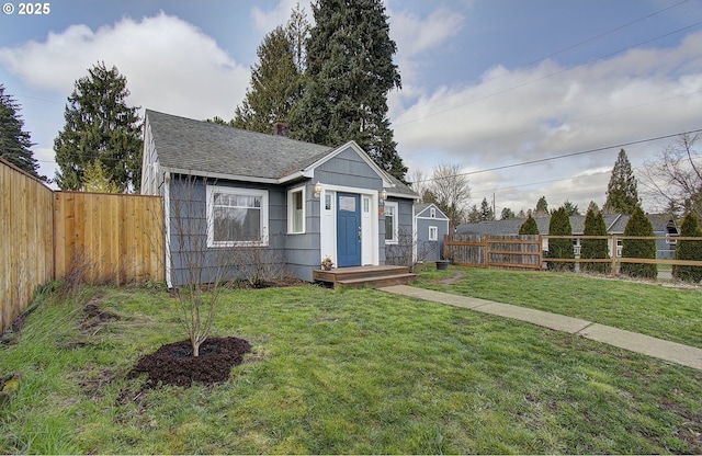 bungalow with a front yard, a fenced backyard, and a shingled roof