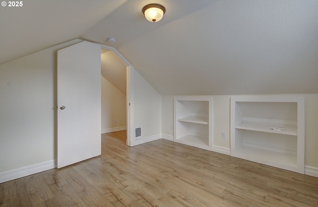 bonus room featuring built in shelves, wood finished floors, visible vents, baseboards, and lofted ceiling