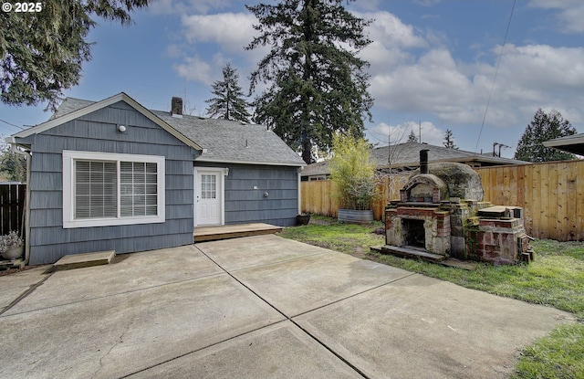 back of property with exterior fireplace, fence, roof with shingles, a chimney, and a patio area