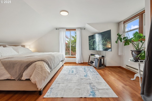 bedroom with light hardwood / wood-style floors, vaulted ceiling, and a baseboard radiator