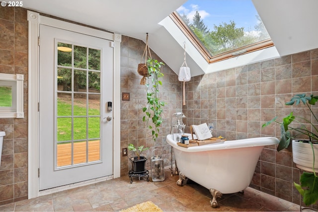 bathroom with a bath, tile walls, and vaulted ceiling with skylight