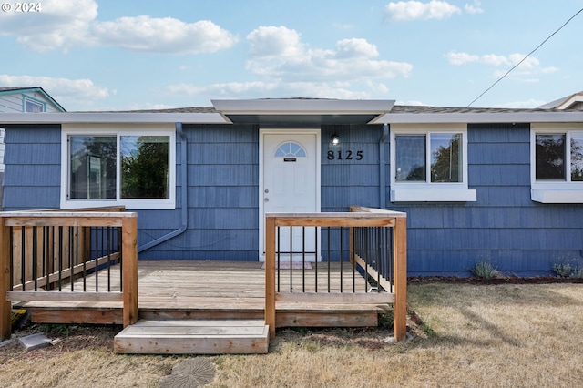 view of exterior entry with a wooden deck and a yard