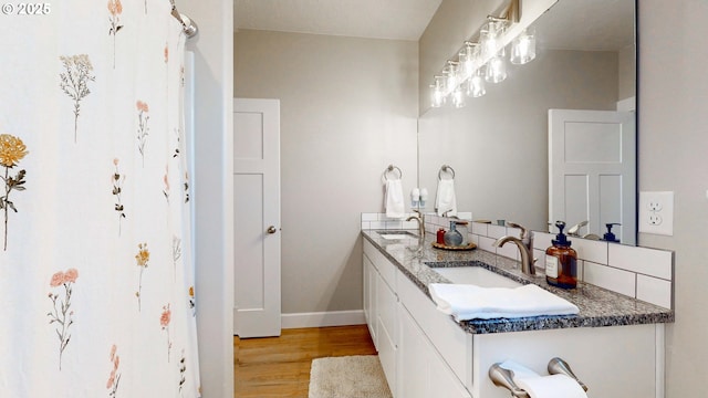 bathroom featuring double vanity, wood finished floors, a sink, and baseboards