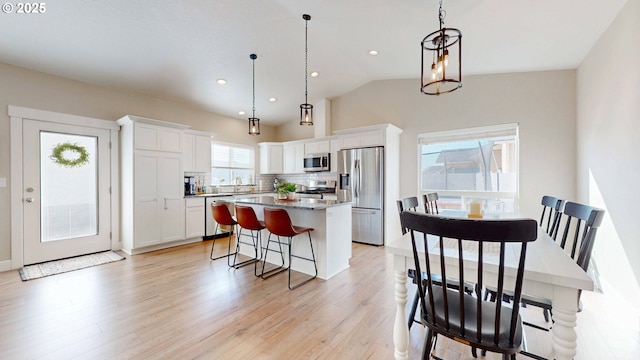 kitchen featuring a center island, stainless steel appliances, white cabinets, light wood-type flooring, and a kitchen bar