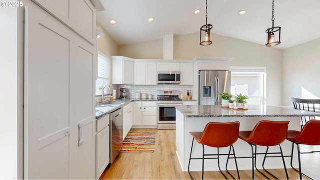 kitchen with light wood-style flooring, stainless steel appliances, a kitchen island, a sink, and a kitchen bar