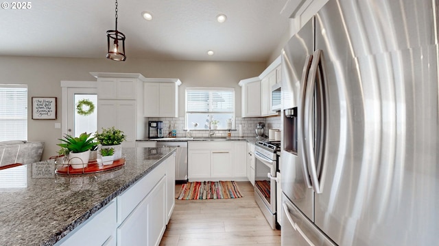 kitchen with white cabinetry, appliances with stainless steel finishes, light wood-type flooring, backsplash, and dark stone counters