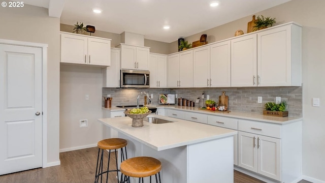 kitchen with dark wood-type flooring, stainless steel microwave, a sink, and white cabinets