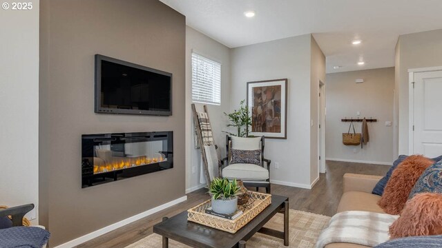 living room featuring a glass covered fireplace, recessed lighting, wood finished floors, and baseboards