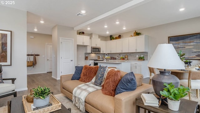 living room featuring baseboards, light wood-type flooring, visible vents, and recessed lighting