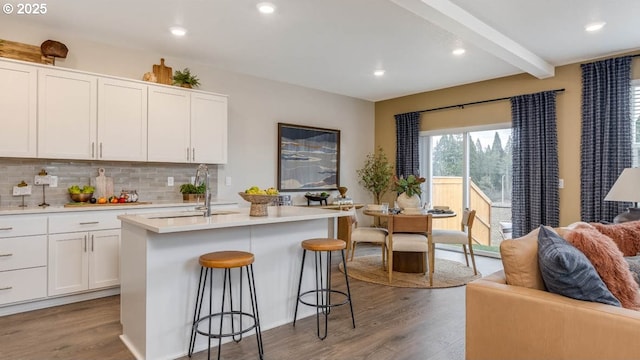 kitchen with wood finished floors, a sink, light countertops, backsplash, and beamed ceiling