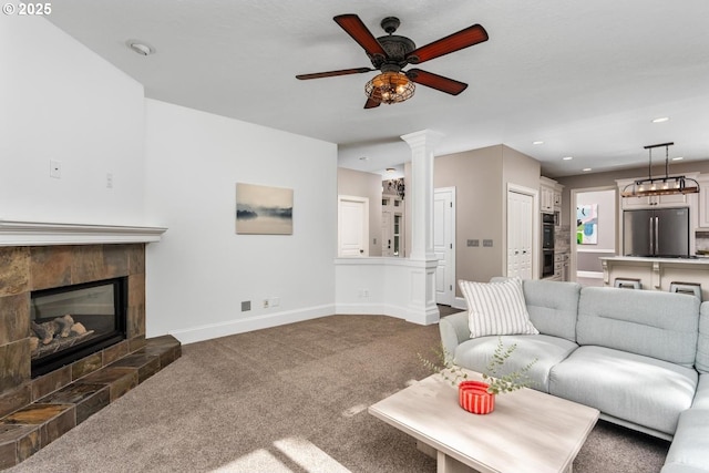 living area with decorative columns, baseboards, a tiled fireplace, ceiling fan, and carpet floors