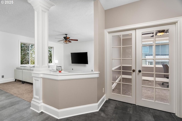 interior space featuring french doors, a ceiling fan, open floor plan, a textured ceiling, and ornate columns