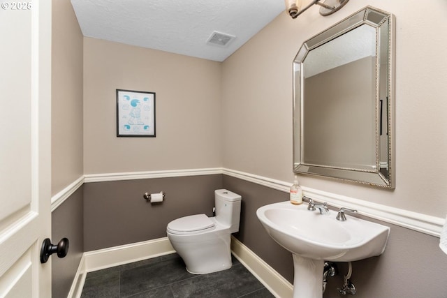 bathroom with a textured ceiling, toilet, visible vents, baseboards, and tile patterned floors