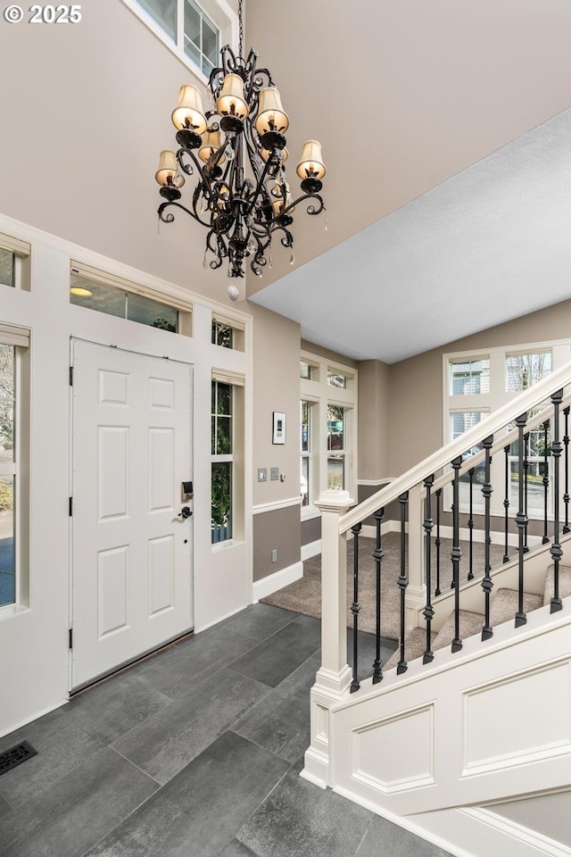 entrance foyer featuring a towering ceiling, stairs, visible vents, and a notable chandelier