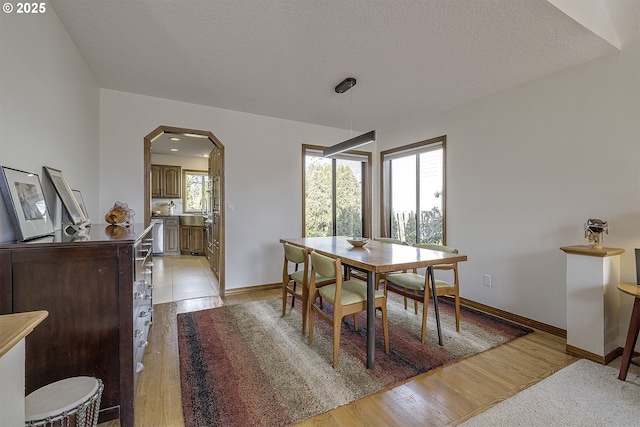 dining room with arched walkways, a textured ceiling, baseboards, and light wood-type flooring