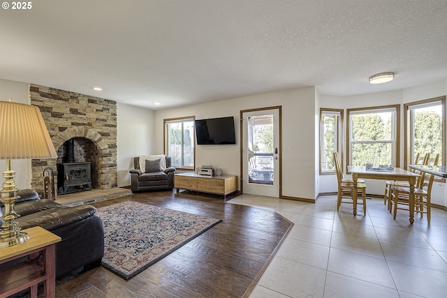 living area featuring a wood stove, light tile patterned floors, baseboards, and a textured ceiling