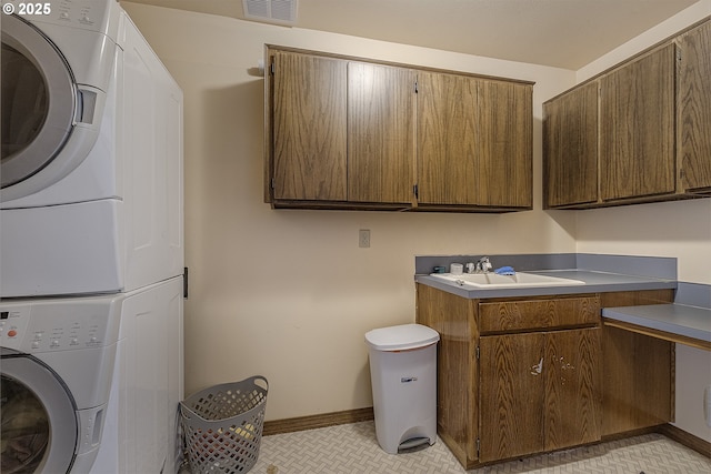 washroom with visible vents, a sink, cabinet space, stacked washer / drying machine, and baseboards