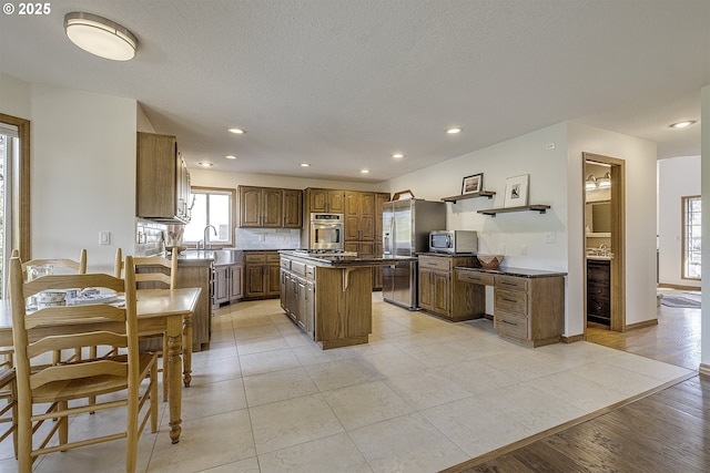 kitchen with dark countertops, appliances with stainless steel finishes, a sink, recessed lighting, and a kitchen island