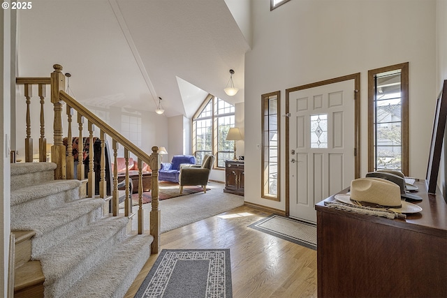 entrance foyer featuring light wood finished floors, high vaulted ceiling, stairs, and baseboards