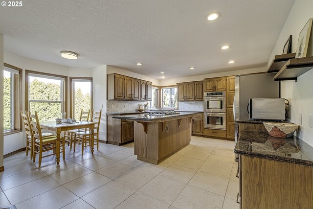 kitchen with a kitchen breakfast bar, a center island, stainless steel double oven, dark stone counters, and decorative backsplash