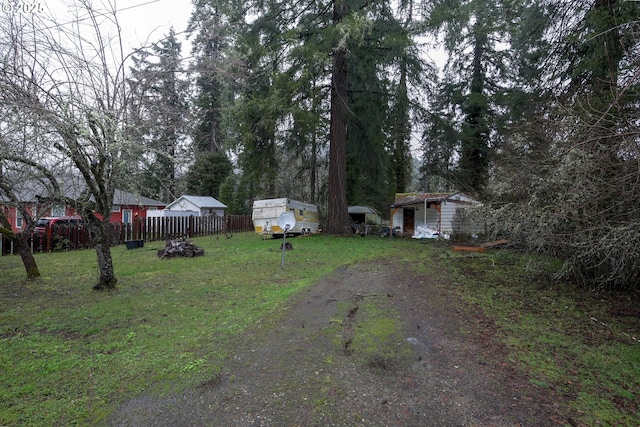 view of yard featuring dirt driveway, an outbuilding, and fence