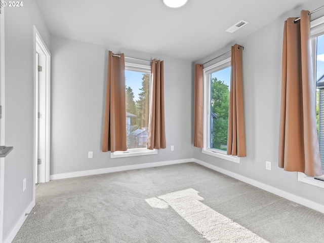 unfurnished room with a healthy amount of sunlight, light colored carpet, visible vents, and baseboards