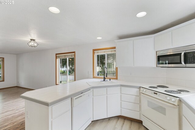 18450 SW Longacre St, Beaverton, OR 97003 - kitchen with white appliances, a peninsula, a sink, light wood-style floors, and white cabinets