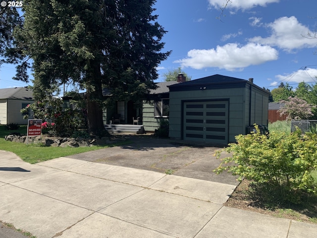 view of front of property featuring concrete driveway, a chimney, a garage, and fence