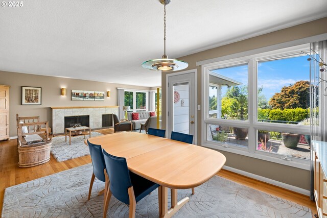 dining area featuring light wood-style floors, a tile fireplace, and baseboards