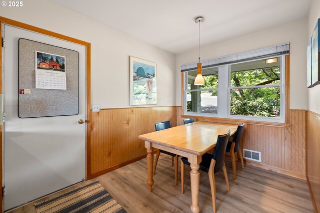 dining area with wainscoting, light wood finished floors, and wooden walls