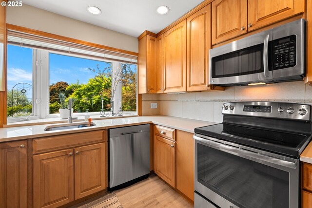 kitchen featuring appliances with stainless steel finishes, a sink, recessed lighting, light countertops, and light wood-style flooring