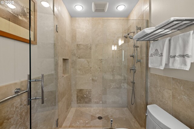 bathroom with toilet, a shower stall, and tile walls