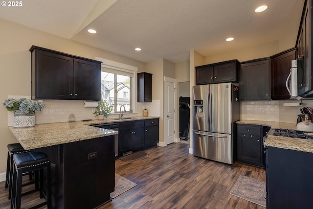 654 Patrol St, Molalla, OR 97038 - kitchen featuring appliances with stainless steel finishes, a sink, a peninsula, light stone countertops, and dark wood-type flooring