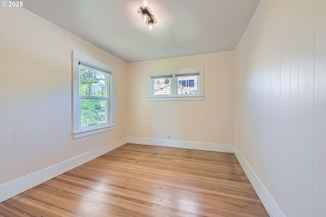 empty room with light wood finished floors, baseboards, ornamental molding, and wood walls