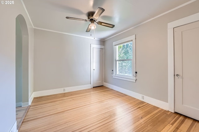 unfurnished bedroom featuring arched walkways, baseboards, light wood-style floors, ceiling fan, and crown molding