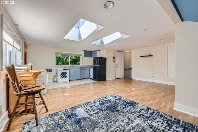 living area with light wood-type flooring, baseboards, visible vents, a skylight, and washer / dryer