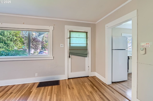 doorway featuring plenty of natural light, light wood-style flooring, visible vents, and ornamental molding