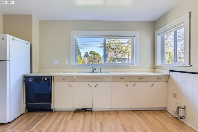 kitchen featuring light wood finished floors, light countertops, freestanding refrigerator, and dishwashing machine