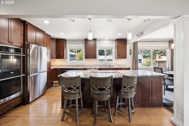 kitchen with a kitchen island, backsplash, appliances with stainless steel finishes, and light wood-style flooring