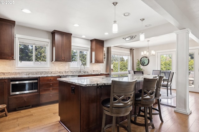 kitchen with light stone countertops, light wood finished floors, stainless steel microwave, decorative backsplash, and a kitchen island